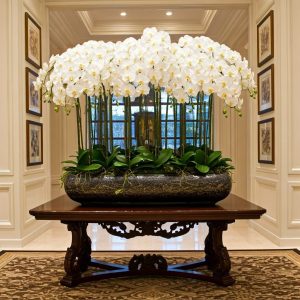 LARGE ARTIFICIAL ORCHID ARRANGEMENT IN A CHINESE STYLE PLANTER ON A LARGE TABLE IN AN ENTRANCE TO A HOME