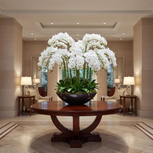 LARGE ARTIFICIAL white ORCHID ARRANGEMENT IN ALARGE PLANTER ON A LARGE TABLE IN AN ENTRANCE TO A HOTEL
